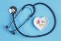 Stethoscope and various pills in a saucer in shape of heart on a blue wooden background Royalty Free Stock Photo