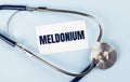 Stethoscope and white card with MELDONIUM text on blue background. Medical concept