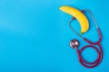 Stethoscope and yellow banana on blue background. For men penis