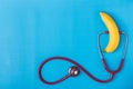 Stethoscope and yellow banana on blue background. For men penis