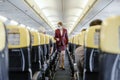 Stewardess with face mask walking in airplane among passengers