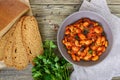 Stewed broad beans in tomato sauce with herbs and spices close-up, slices of rye bread Royalty Free Stock Photo