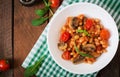 Stewed white beans with mushrooms and tomatoes with spicy sauce in a white bowl.