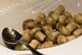 Stewed whole champignon mushrooms in a white bowl with a silver