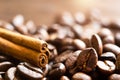 A stick of cinnamon lies on the roasted coffee beans close-up - fragrant macro backgrounds. Brown arabica coffee beans are