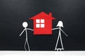 Stick couple figure together holding a red house cutout in black background. Home ownership, housing loan concept.