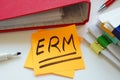 A sticky note ERM Enterprise Risk Management with an abbreviation next to a pile of papers. Royalty Free Stock Photo