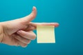 Sticky note, finger up of thumb, yellow reminder on blue background. Royalty Free Stock Photo