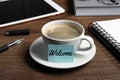 Sticky note with word Welcome attached to cup of coffee on wooden office desk Royalty Free Stock Photo