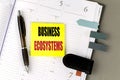 Sticky note with the words business ecosystems on open planner with pen and bookmarks on desk Royalty Free Stock Photo