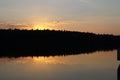 A still dark moody lake at dusk reflects the setting sun on the water surface with a silhouette of trees