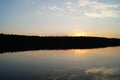 A still dark moody lake at dusk reflects the setting sun on the water surface with a silhouette of trees