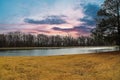 A still green lake surrounded by yellow winter grass in the park with powerful purple and red clouds at sunset Royalty Free Stock Photo