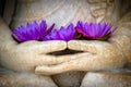 purple flowers sit in a buddha's hands as if they are holding a statue