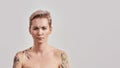 Still kind of miffed. Portrait of dissatisfied half naked tattooed woman with pierced nose and short hair frowning face