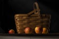 Still life of apples next to a vintage picnic basket against a black background Royalty Free Stock Photo