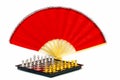 Chess board and pieces with red oriental bamboo folding fan on white background 