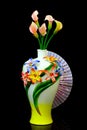 Beautiful pink calla lilly flowers in a decorative porcelain vase with a folding fan against black background