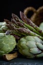 A still life of artichokes with knife and asparagus on the rustic textured background close dramatic view