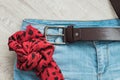 Still life of blue jeans with a brown leather belt on a light wood background