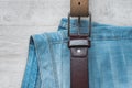 Still life of blue jeans with a brown leather belt on a light wood background