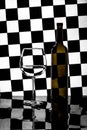 Still life with a bottle and a glass on a background of black and white squares Royalty Free Stock Photo