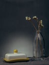 Still life of a bouquet of dried flowers in a glass bottle and butter in a yellow dish on a table with gray linen napkin