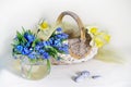 Beautiful bouquet of spring flowers in a vase with water and a basket on a table on a brown background