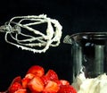 A still life with a bowl of fresh an red strawberries, a food processor, mixer whose wire wisks are full of cream, beside a beaker