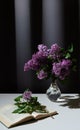 Still life of bright branch of lilac in the glass vase with open book on white table on grey curtains background