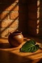 Still life captures a brown ceramic pot and vibrant green leaf on a wood surface with shadow Royalty Free Stock Photo