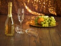 Still life with champagne and two glasses and plate with fresh fruits orange, green grapes, on a wooden table, Golden glittery Royalty Free Stock Photo