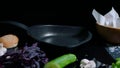 Still life of chef`s table on black surface. Pan, knife, fresh vegetables and ingredientes for dish