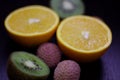 Still life of citrus, juicy kiwi and orange in the cut and Litchi chinensis on a dark background