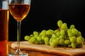 Still life of cluster of white grapes on a wooden board. Glass and bottle of white wine. Black background. Wine making concept Royalty Free Stock Photo