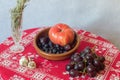 Still life composed of blueberries, black grapes, tomatoes, garlic, and a branch of fresh rosemary on a red Christmas tablecloth.