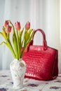 Still life composition, in home interior on the table with a tablecloth, tulips in a beautiful vase on a background of red ladies` Royalty Free Stock Photo