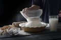 Still life on dark wooden surface. Flour sifting process. Dough ingredients next to bowl with flour.