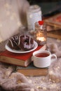 Still life details in home interior of living room. Cup of tea and chocolate donuts on stack of book. Tea leisure time in autumn