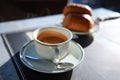 Elegant white ceramic cup of freshly brewed espresso coffee with foam on saucer. Blurred crispy croissants on background Royalty Free Stock Photo