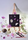 Still life with empty mock up  black sketchbook on a wooden easel, scattered pencils and pens, strewn pink flowers and steaming co Royalty Free Stock Photo