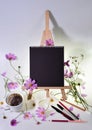 Still life with empty black sketchbook on a wooden easel, scattered pencils and pens, strewn pink flowers and steaming co Royalty Free Stock Photo