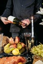 Still life with food, fruits, flowers and candles on a black background. Renaissance style. A man pours wine in a crysta