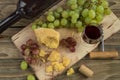 Still life from food and wine. The piece of hard cheese lies on a chopping board. Clusters of red and green mature grapes, a dark Royalty Free Stock Photo