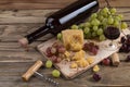 Still life from food and wine. The piece of hard cheese lies on a chopping board. Clusters of red and green mature grapes, a dark Royalty Free Stock Photo