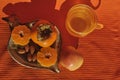 Persimmons and tangerine and almonds on a clay saucer. A cup and an apple on a napkin background, healthy fo