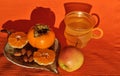 Persimmons and tangerine and almonds on a clay saucer. A cup and an apple on a napkin background, healthy fo