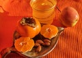 Persimmons and tangerine and almonds on a clay saucer. A cup and an apple on a napkin background, healthy fo