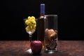 Still life of a glass with grapes, an apple,a bottle and a glass of potpourri sitting on wooden table with black background Royalty Free Stock Photo