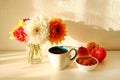 Still life with glass vase with colorful flowers of peonies, cup of tea, apple jam and apples on the white table. Royalty Free Stock Photo